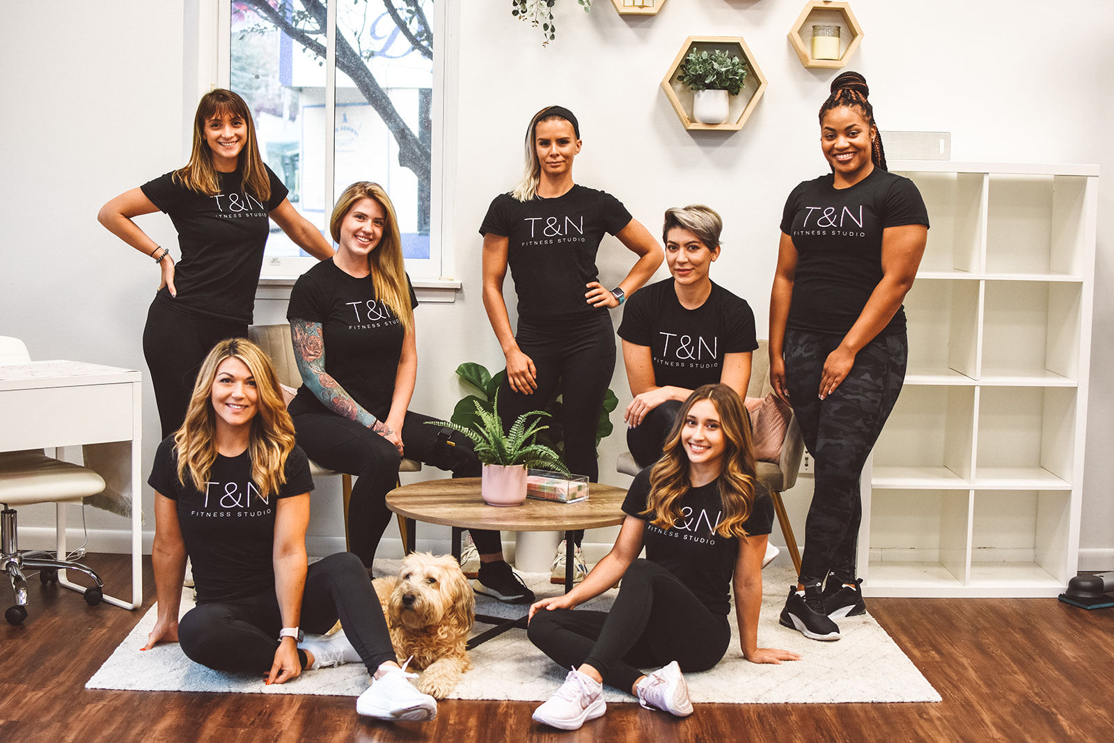 Find a group of women posing with a dog while wearing black t-shirts.
