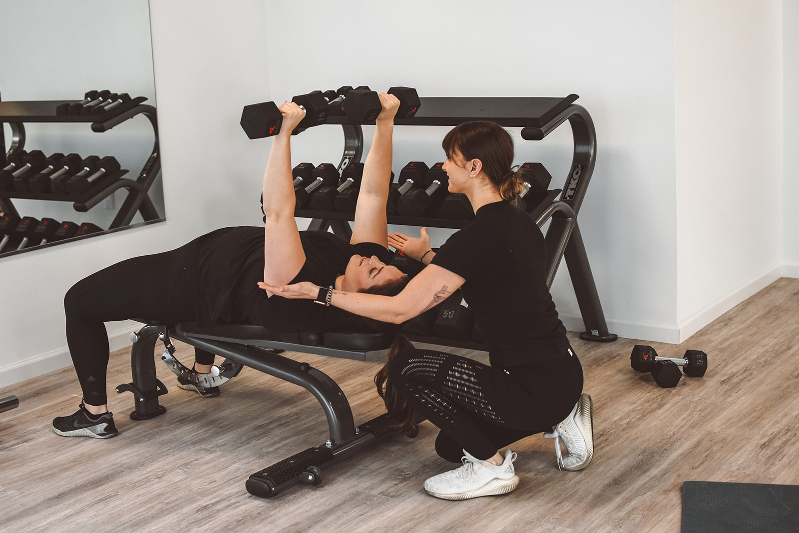 Two women engaging in personal training at a fitness studio with dumbbells.