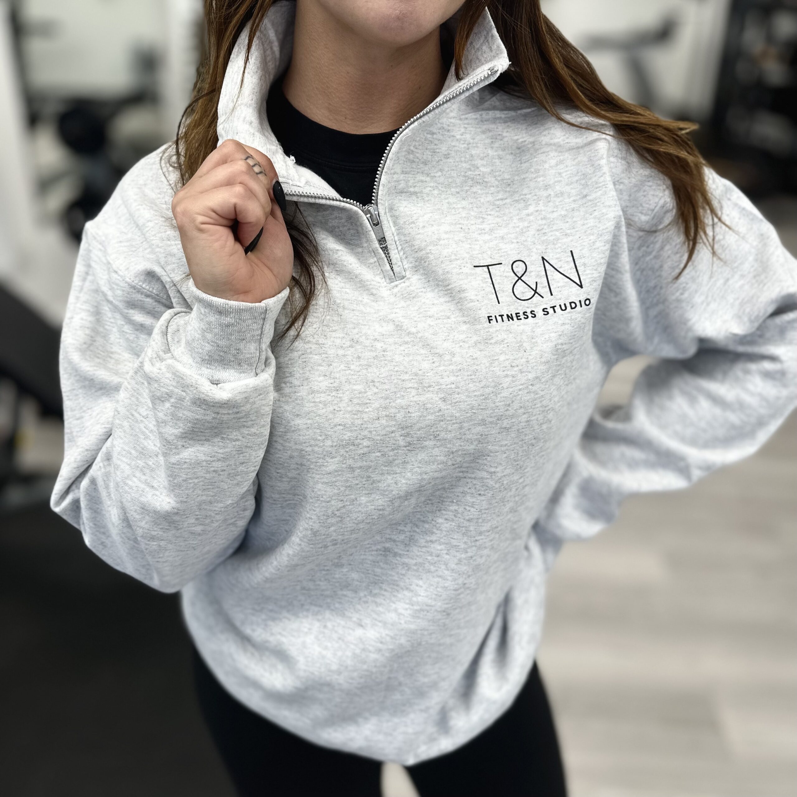 A woman in a fitness studio wearing a grey sweatshirt with merchandise