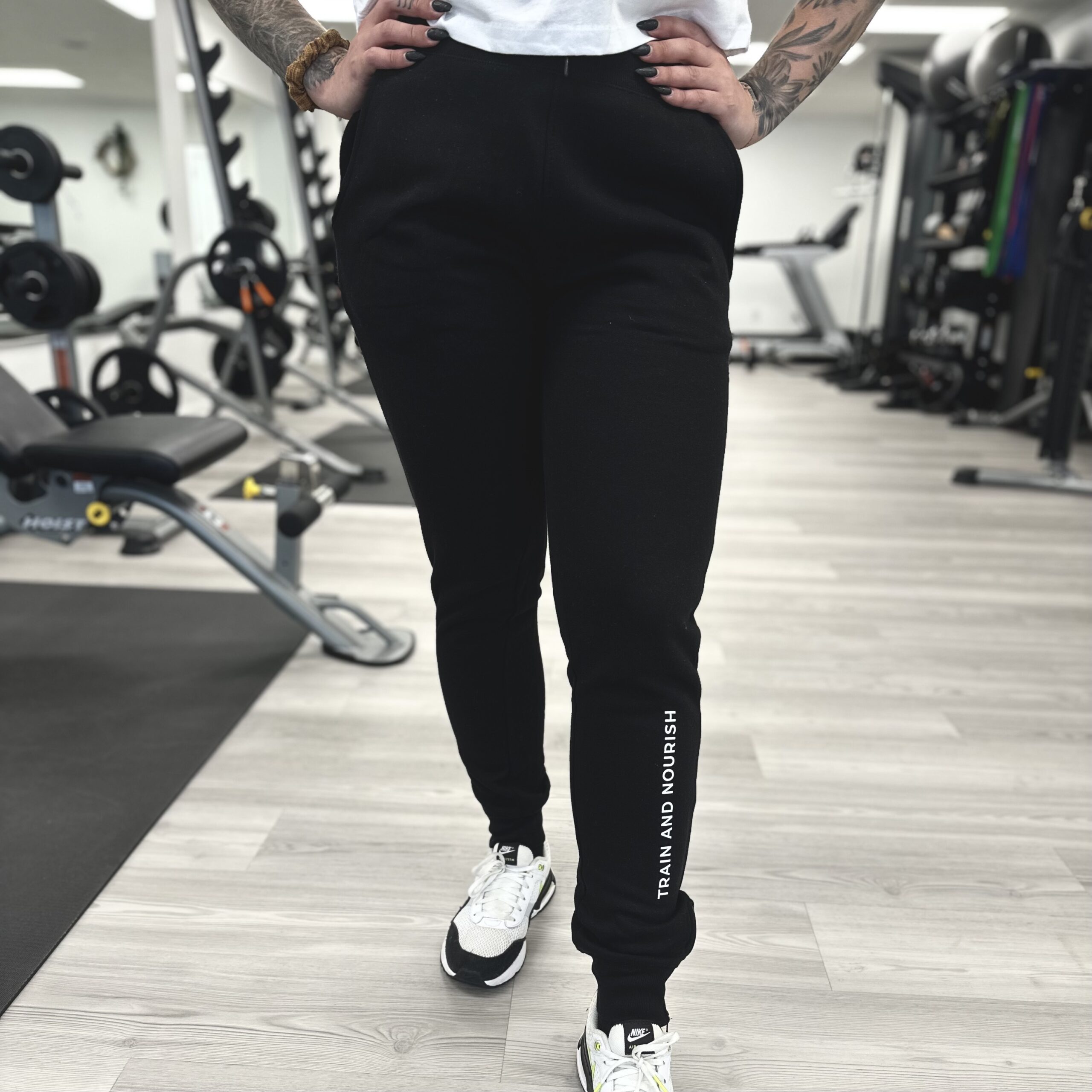 A woman showcasing merchandise in a gym wearing black joggers.