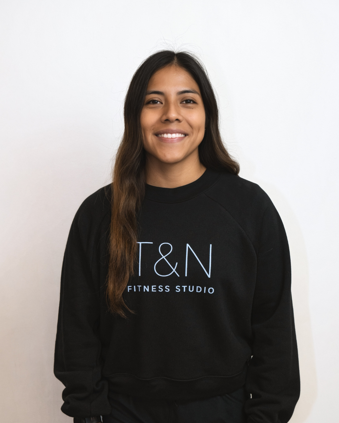 A woman wearing a black sweatshirt with the words t & n fitness studio is part of a Team.