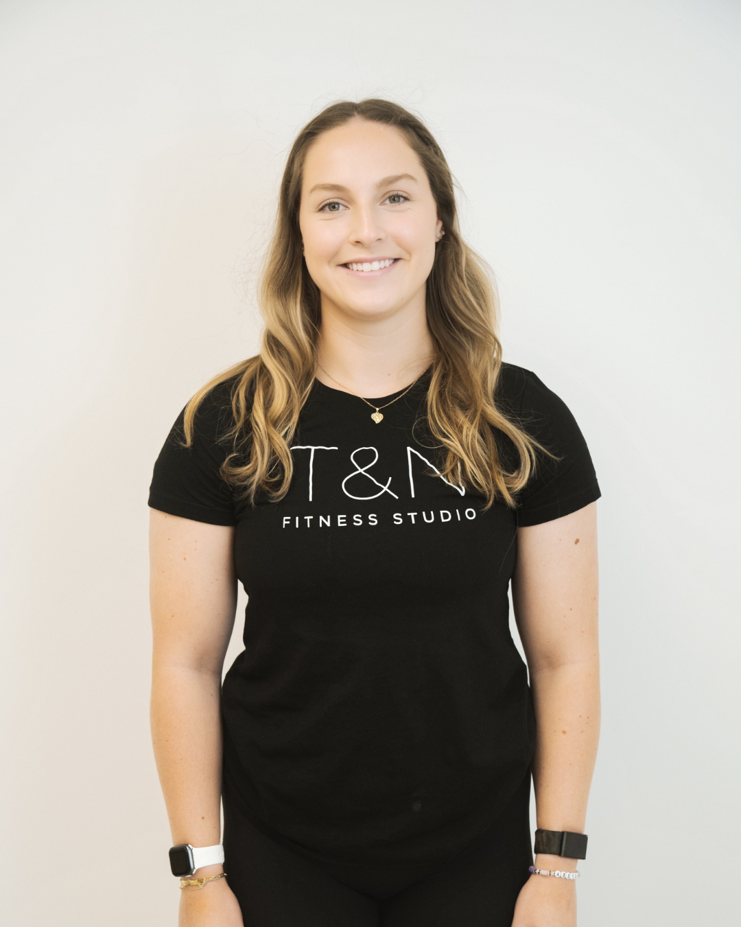 A woman wearing a black t-shirt stands confidently in front of a white wall, embodying the essence of team spirit and showcasing her expertise in SEO keywords.
